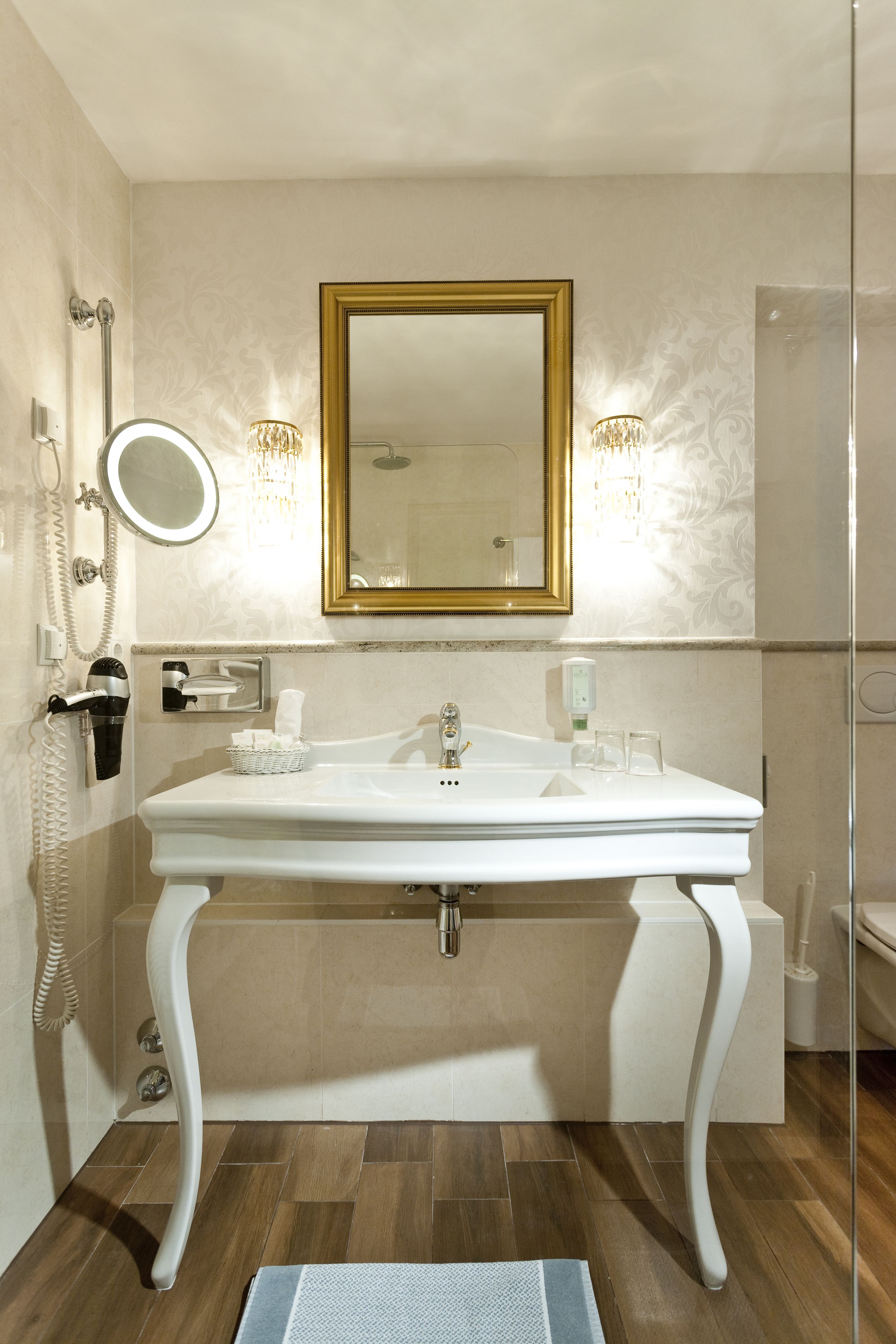 A bathroom with a white sink, gold-framed mirror, and a telephone.