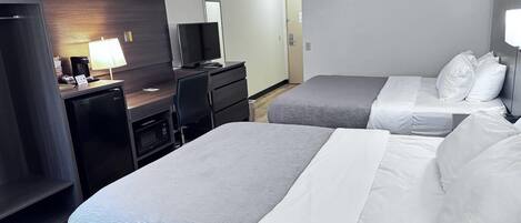 Habitación de hotel con dos camas, un escritorio con computadora, cafetera y televisión.