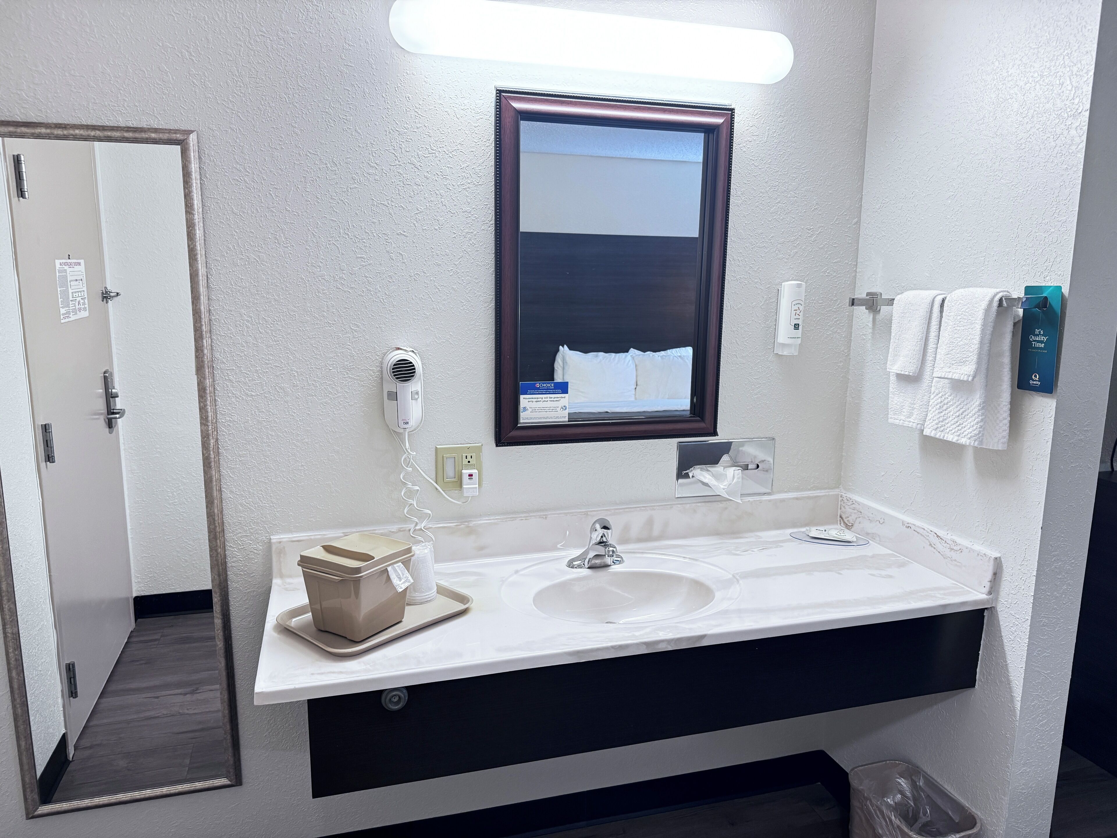 A hotel bathroom with a sink, mirror, towel rack, and a hairdryer on the wall.