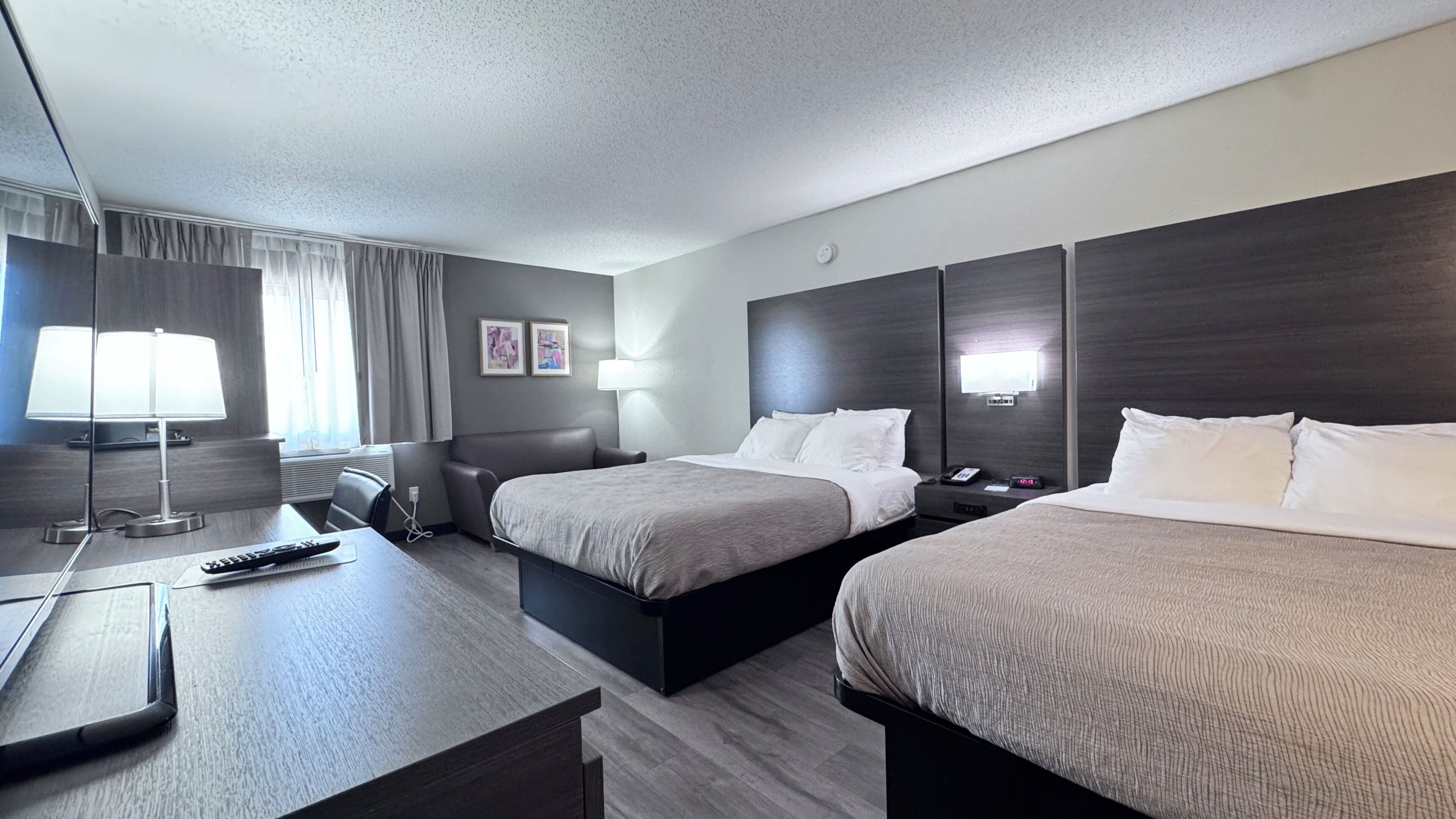 A hotel room with two beds, a desk with a lamp, a TV, and a bedside table with a phone.