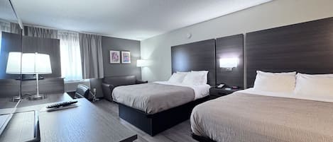 Habitación de hotel con dos camas, un escritorio con lámpara, televisor y mesita de noche con teléfono.