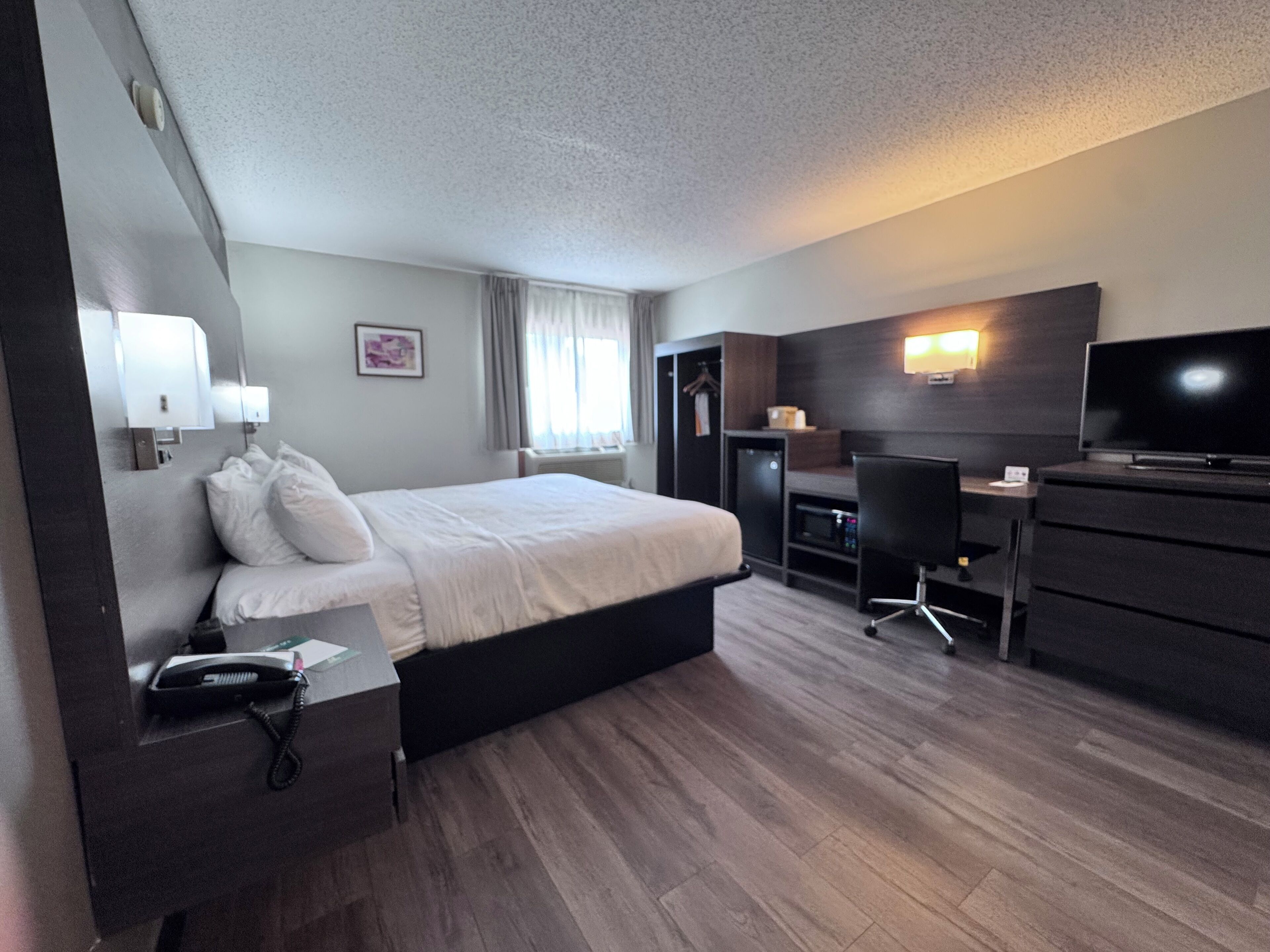 A hotel room with a bed, bedside table, desk, chair, television, and a wardrobe.
