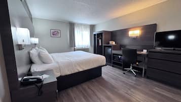 A hotel room with a bed, bedside table, desk, chair, television, and a wardrobe.