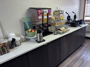 Mostrador de desayuno con cereales, rosquillas, magdalenas y una máquina de café.