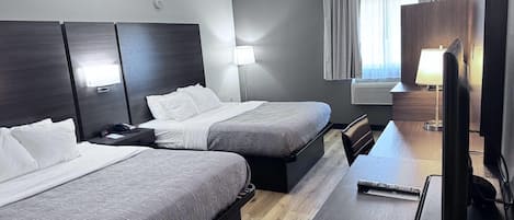 A hotel room with two beds, a desk, a chair, a lamp, and a television.