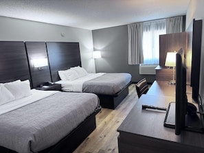 Habitación de hotel con dos camas, un escritorio, una silla, una lámpara y un televisor.
