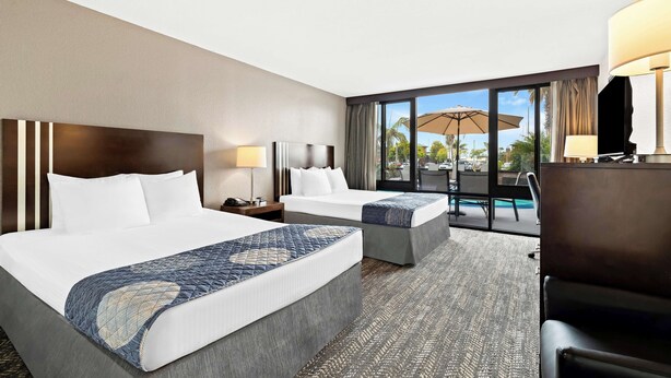 Habitación de hotel con dos camas, un escritorio, una silla y un amplio ventanal con vistas al exterior.