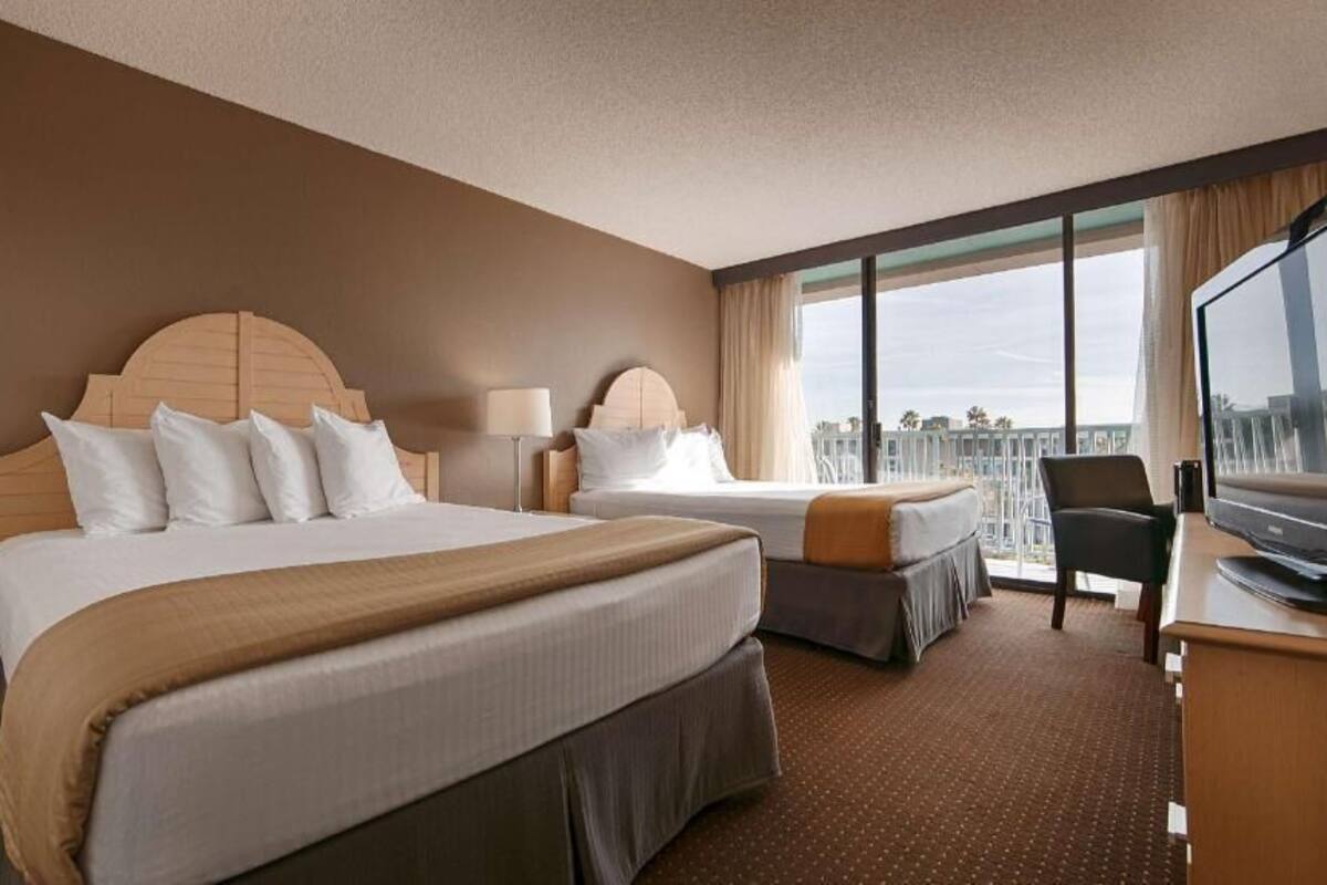 A hotel room with two beds, a desk, a chair, and a television.