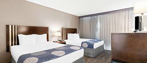 A hotel room with two beds, a desk, a lamp, and a large window with curtains.
