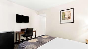 A hotel room with a bed, a desk with a chair, a television mounted on the wall, and a framed picture on the wall.