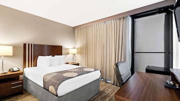 Een hotelkamer met een groot bed, nachtlampjes, een bureau en uitzicht op de omgeving door een raam met gordijnen.