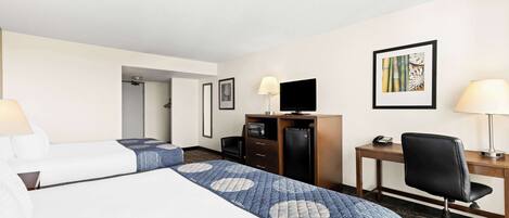 A hotel room with two beds, a desk, a chair, a TV, and a desk lamp.