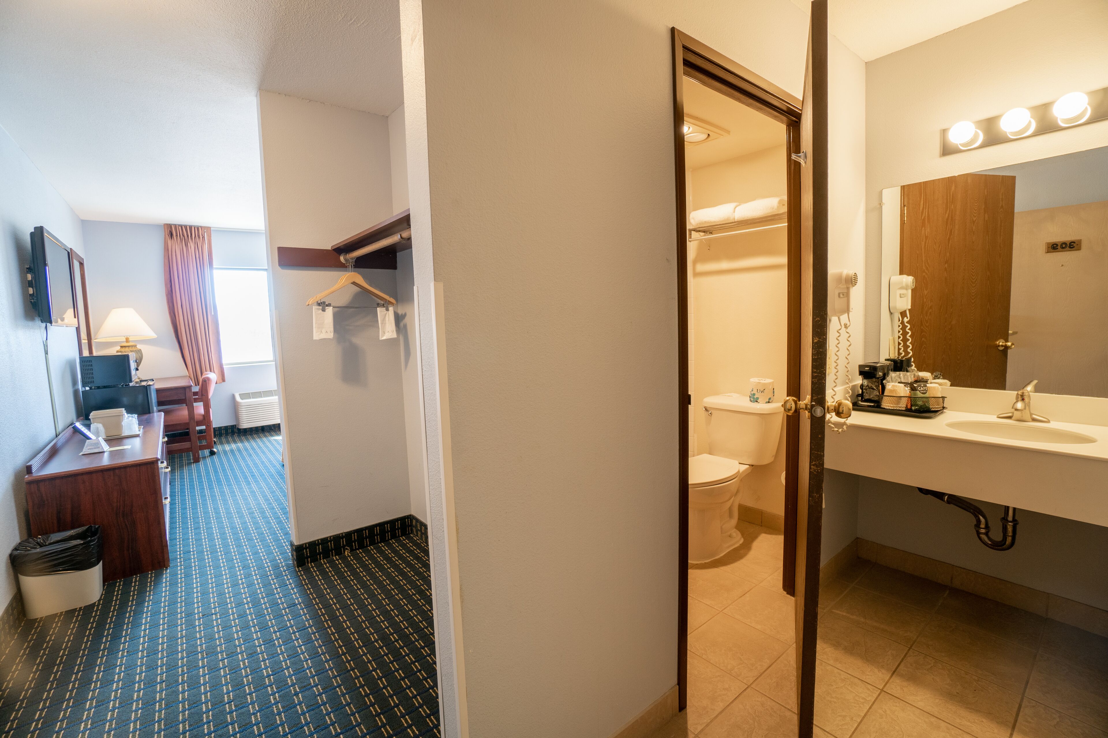 A hotel room with a desk, chair, and a bathroom with a sink and mirror.