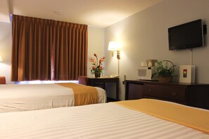 A hotel room with two beds, a desk with a microwave, a TV, and a lamp.