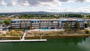 A multi-story hotel with 'Clover Island Inn' signage, a swimming pool, and a dock extending into a body of water. - Clover Island Inn (Kennewick)