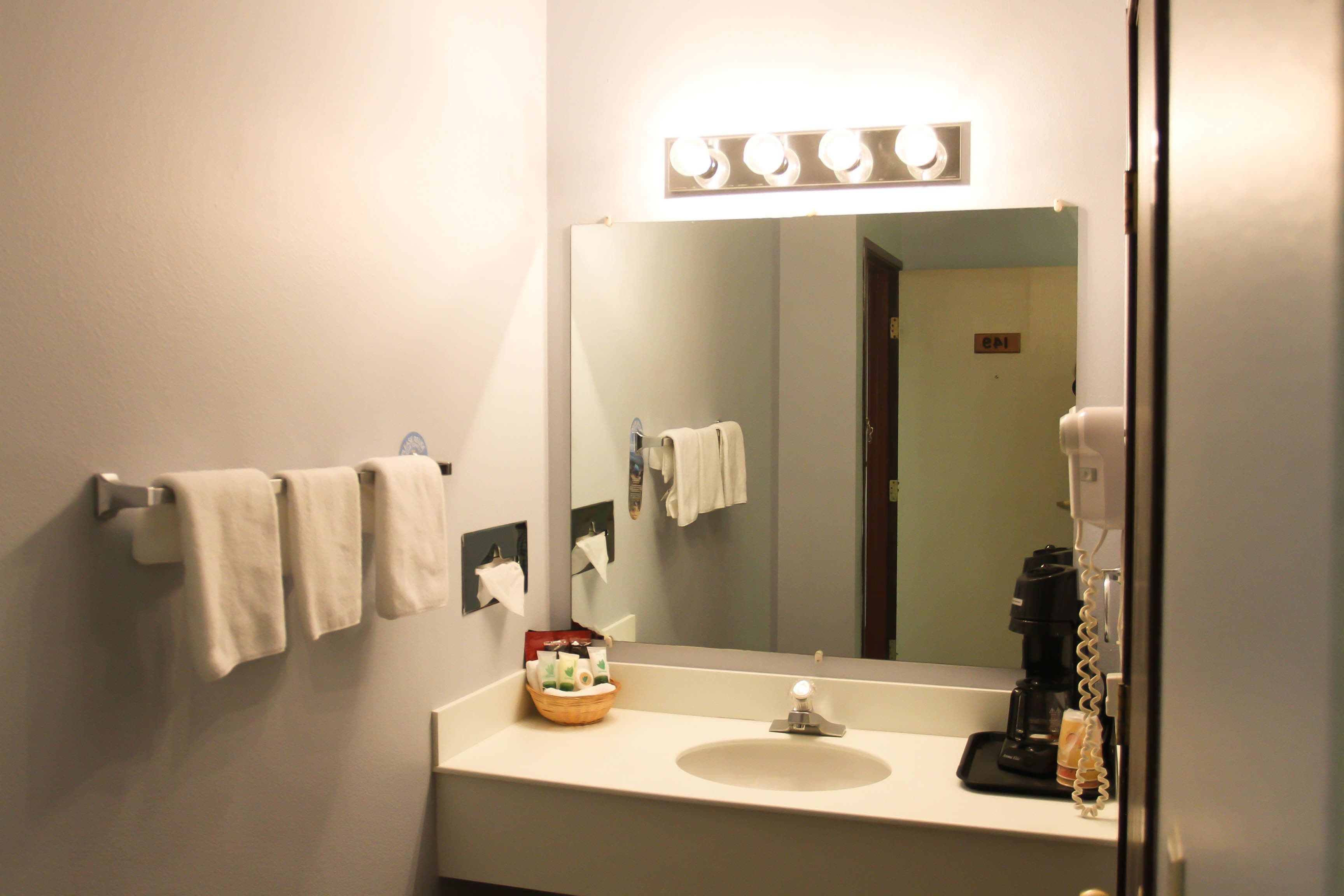 Baño con lavamanos, espejo, toallero y cafetera.