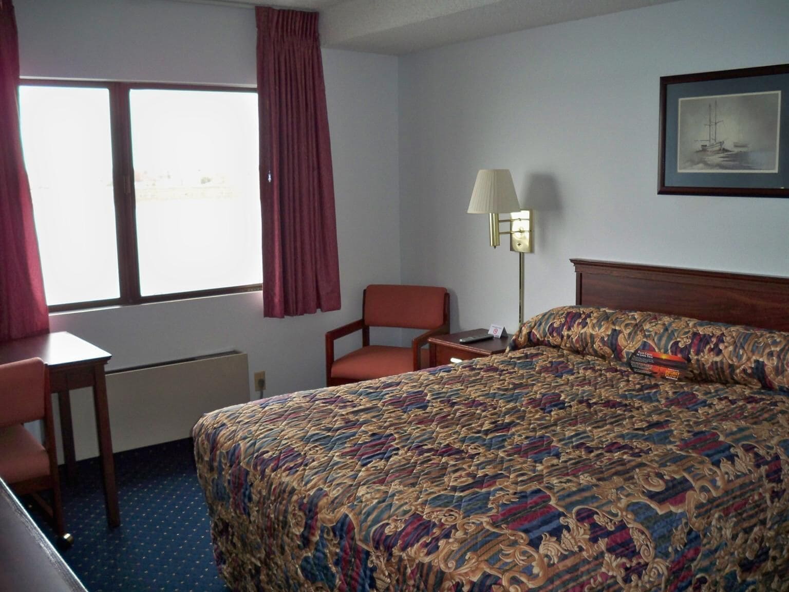 Een hotelkamer met een groot bed, een bureau, een stoel, een lamp en een raam met gordijnen.