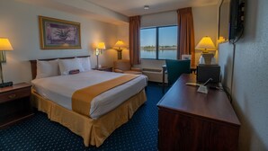A hotel room with a large bed, two bedside tables with lamps, a desk with a computer, and a large window with a view of the water. - Clover Island Inn (Kennewick)