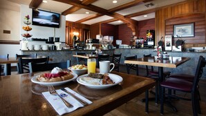 A restaurant with wooden tables and chairs, breakfast plates with pancakes, eggs, and bacon, and a television mounted on the wall. - Clover Island Inn (Kennewick)