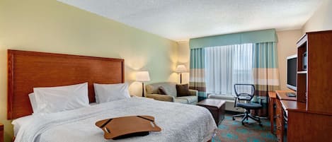A hotel room with a large bed, a desk, a chair, a TV, and a window with curtains.