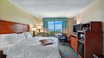 Quarto de hotel com cama, escrivaninha, televisão e vista para o exterior.