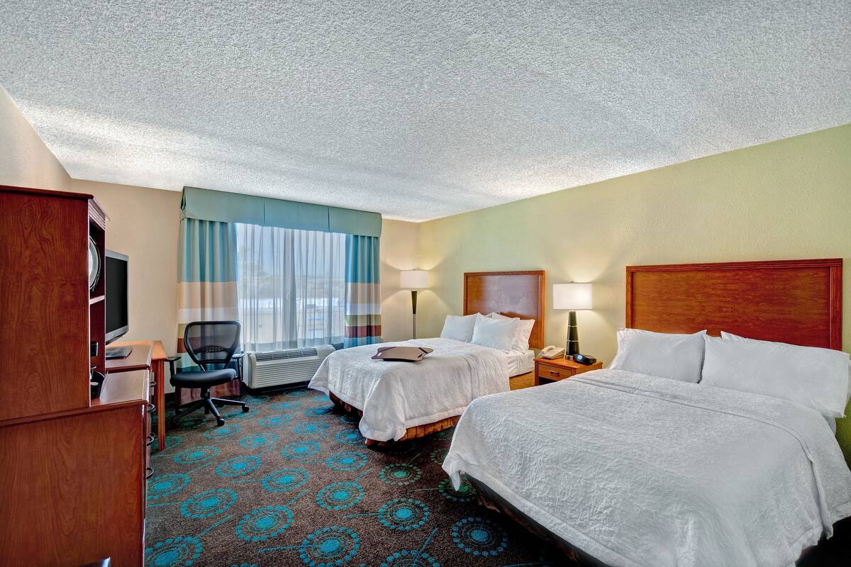 Une chambre d’hôtel avec deux lits, un bureau avec un ordinateur, une chaise et un téléviseur.
