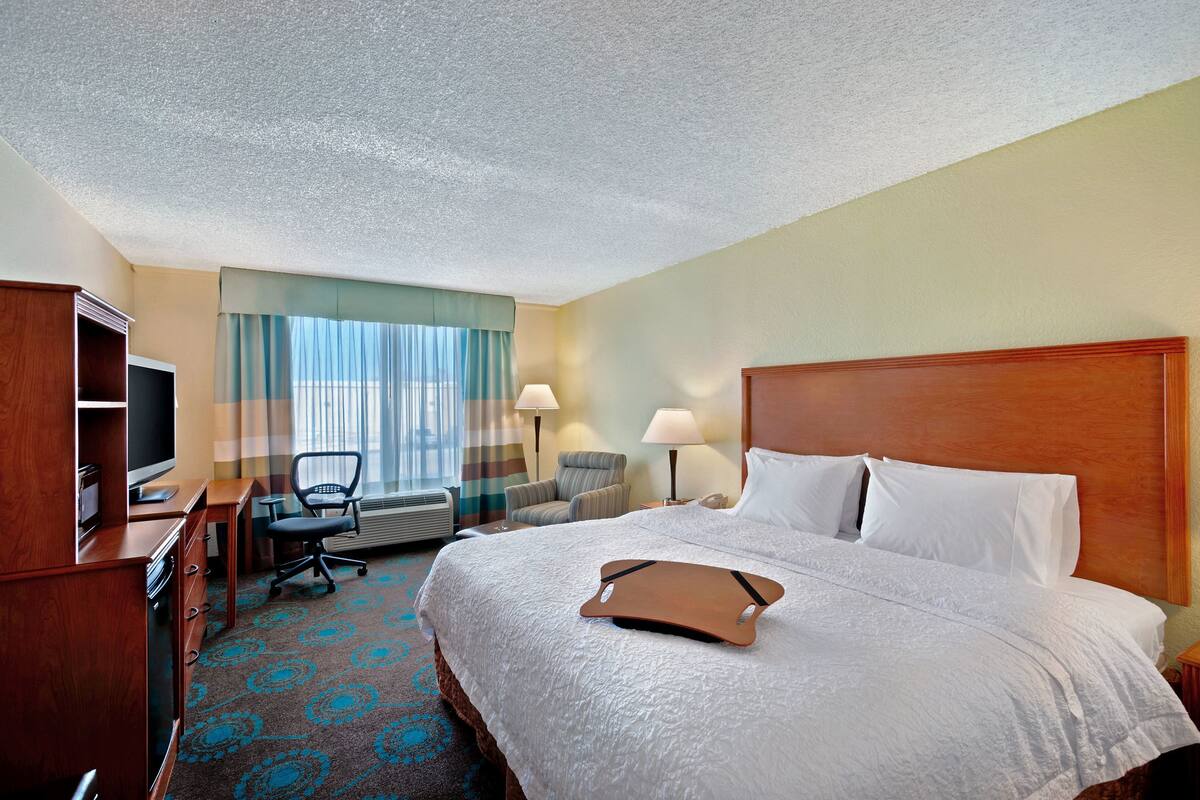 Une chambre d’hôtel avec un grand lit, un bureau avec un ordinateur, une chaise et un téléviseur.