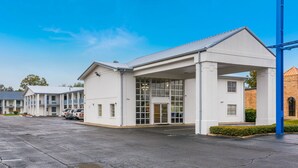 A building with a covered entrance, a parking lot, and a row of similar buildings in the background. - Motel 6 Alexandria, LA - South (Alexandria)