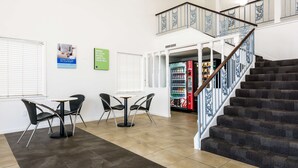 A lobby with a staircase, a Coca-Cola vending machine, and two tables with chairs. - Motel 6 Alexandria, LA - South (Alexandria)