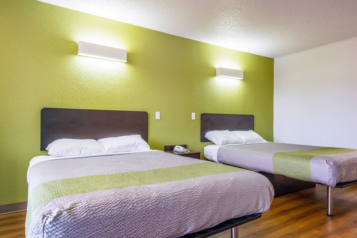 Two single beds with headboards, a bedside table with a lamp, and a wall-mounted light fixture.