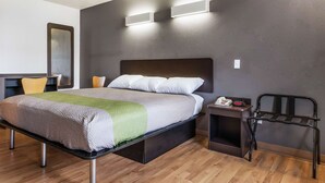 A modern hotel room with a large bed, bedside table, and a chair. - Motel 6 Alexandria, LA - South (Alexandria)