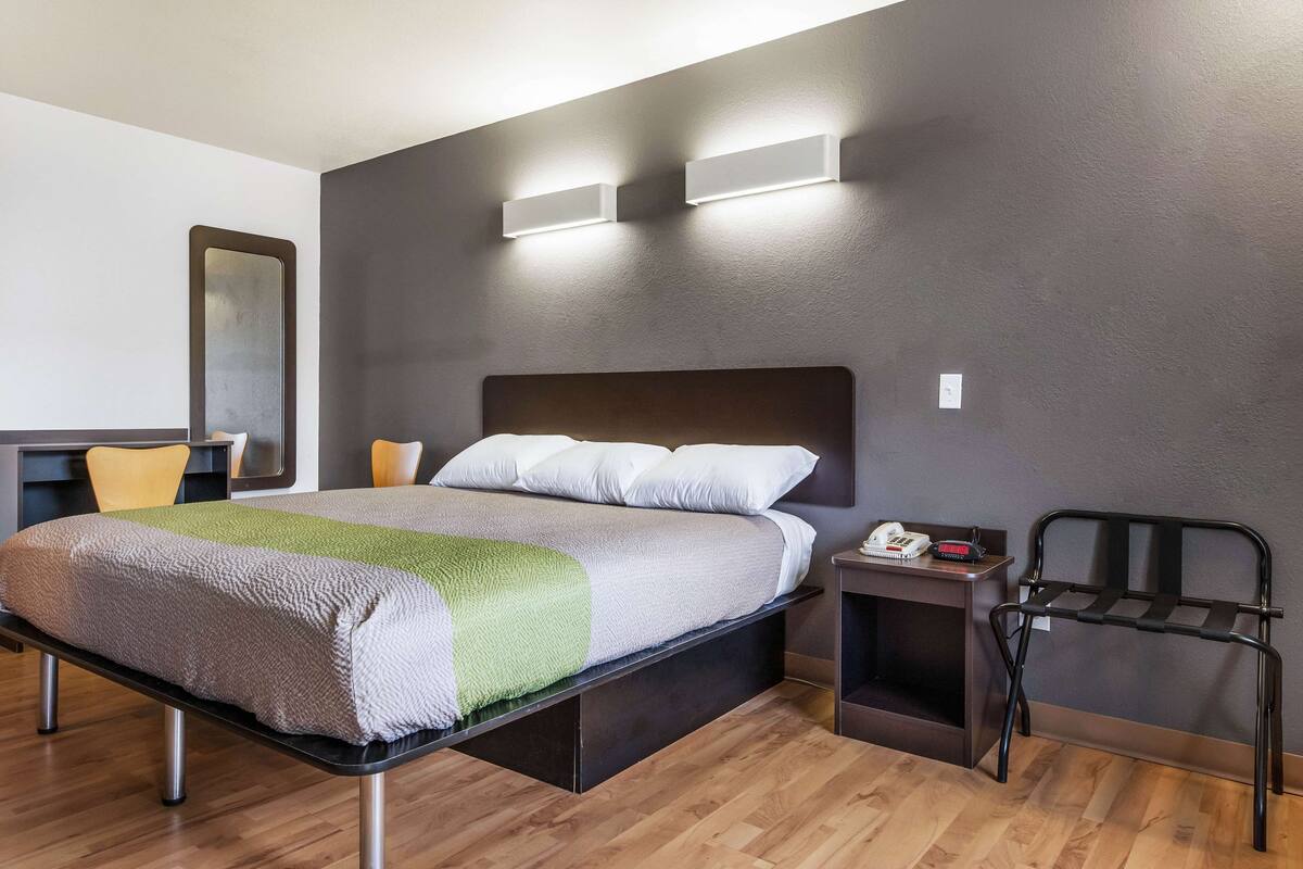 A modern hotel room with a large bed, bedside table, and a chair.