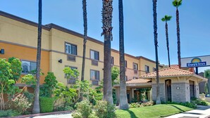 A Days Inn hotel with a yellow facade, palm trees, and a clear blue sky. - Days Inn by Wyndham West Covina (West Covina)