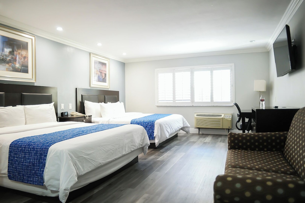 A hotel room with two beds, a desk, a chair, a TV, and a window.