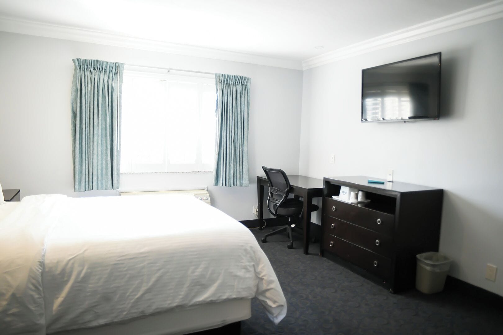 Ein Hotelzimmer mit einem Bett, einem Schreibtisch, einem Sessel, einem Fernseher und einem fenster mit Vorhängen.