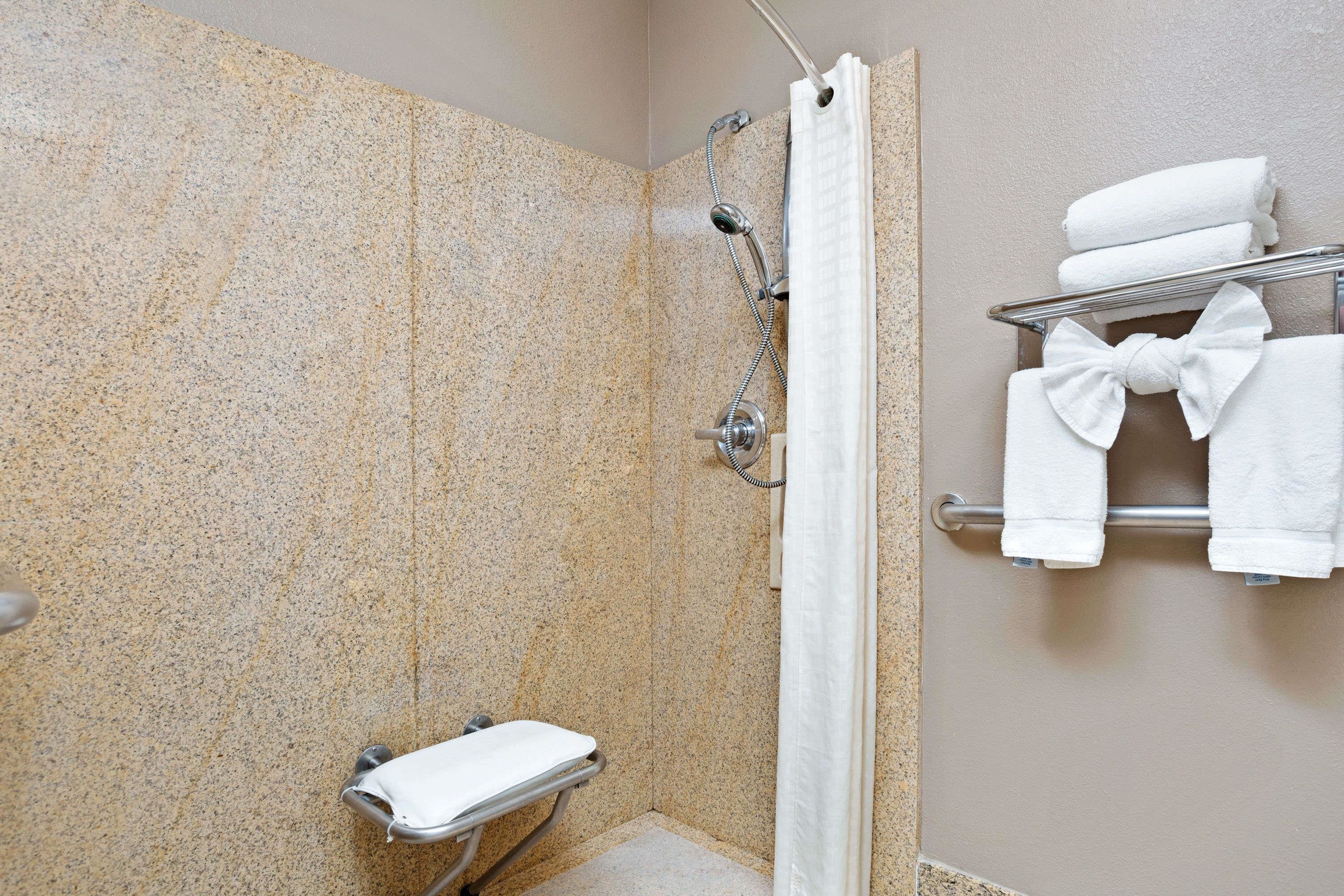 A shower area with a granite wall, a showerhead, a towel rack with folded towels, and a small bench.
