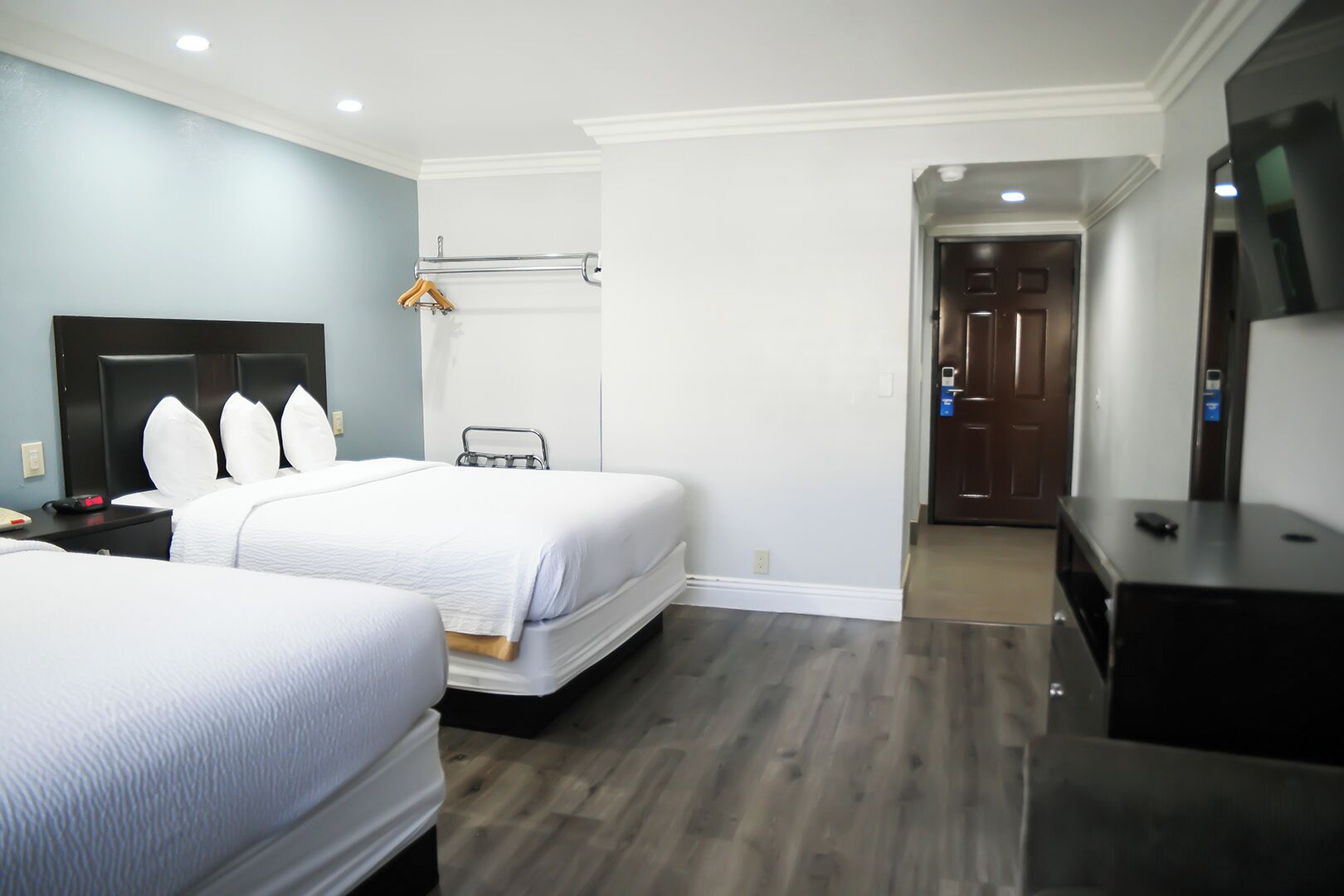A hotel room with two beds, a desk, a TV, and a door leading to another room.