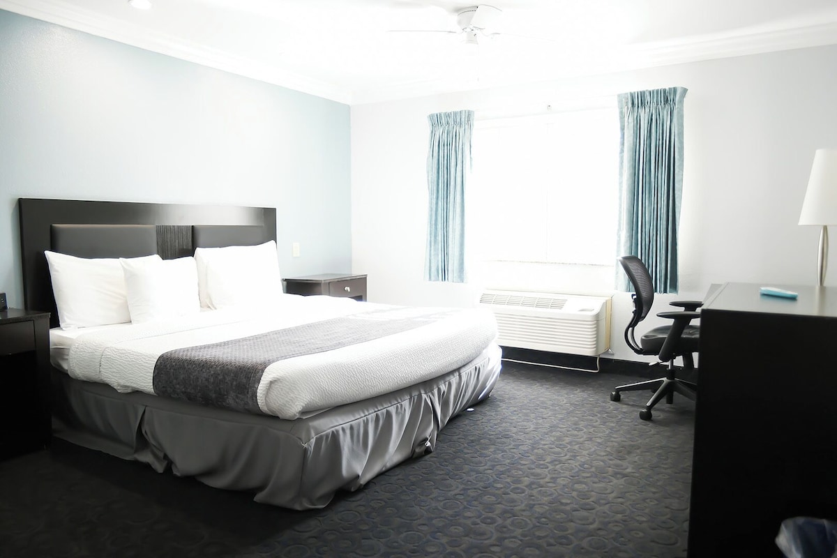 A hotel room with a bed, a desk, an air conditioner, and curtains.