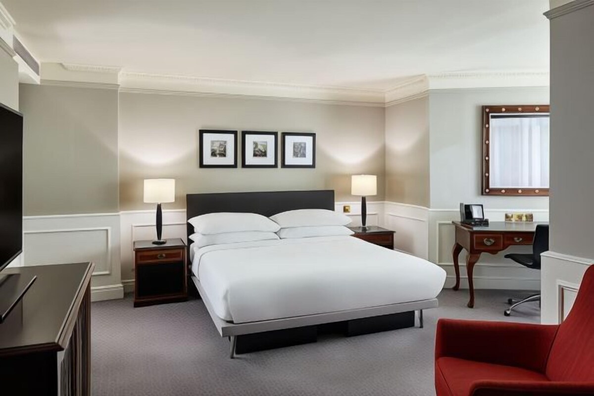 A hotel room with a bed, bedside tables, a desk, a chair, and a television.
