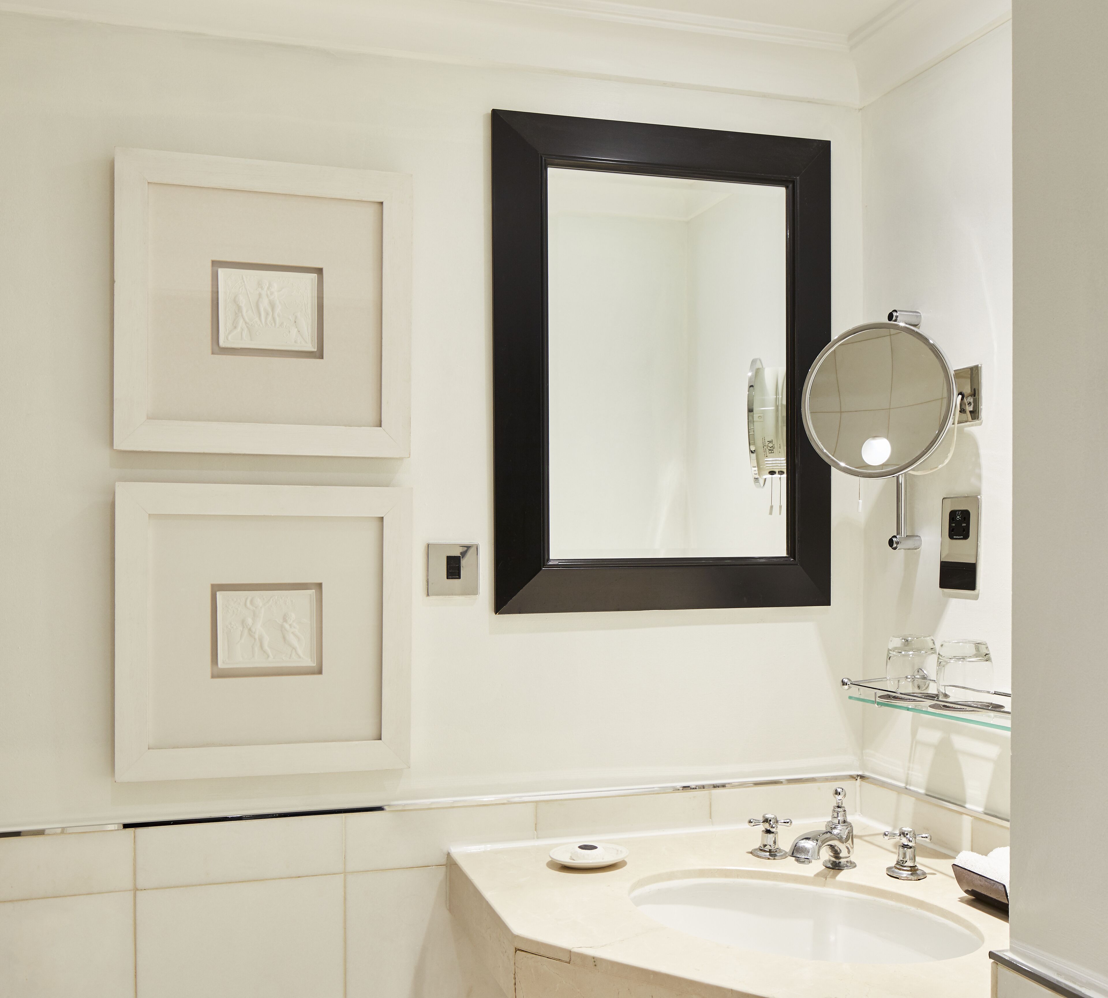 A bathroom with a white sink, a mirror with a black frame, and two framed artworks on the wall.