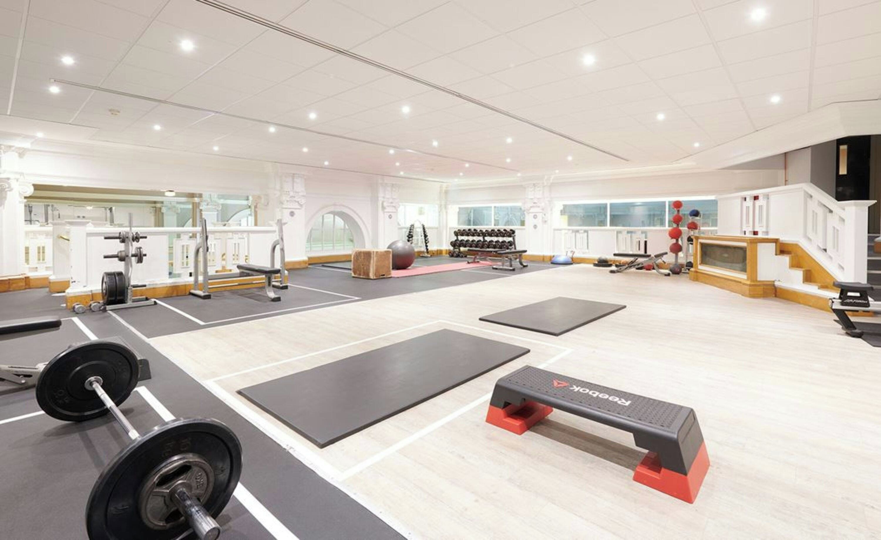 A gym with weightlifting equipment, exercise mats, and dumbbells.