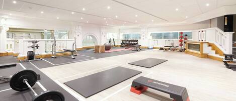 A gym with weightlifting equipment, exercise mats, and dumbbells.