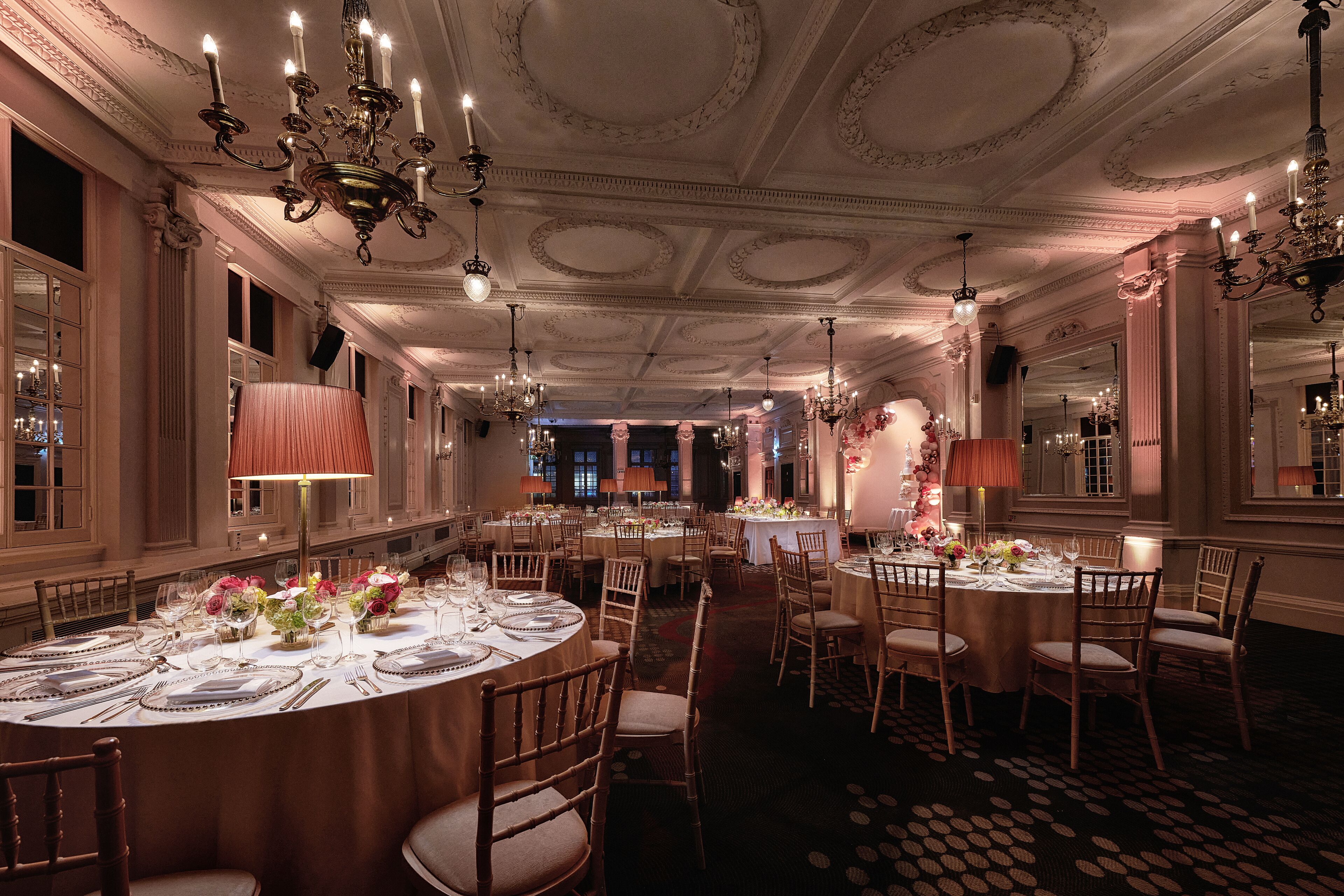 A grand dining hall with ornate chandeliers, round tables set for dining, and elegant floral centerpieces.