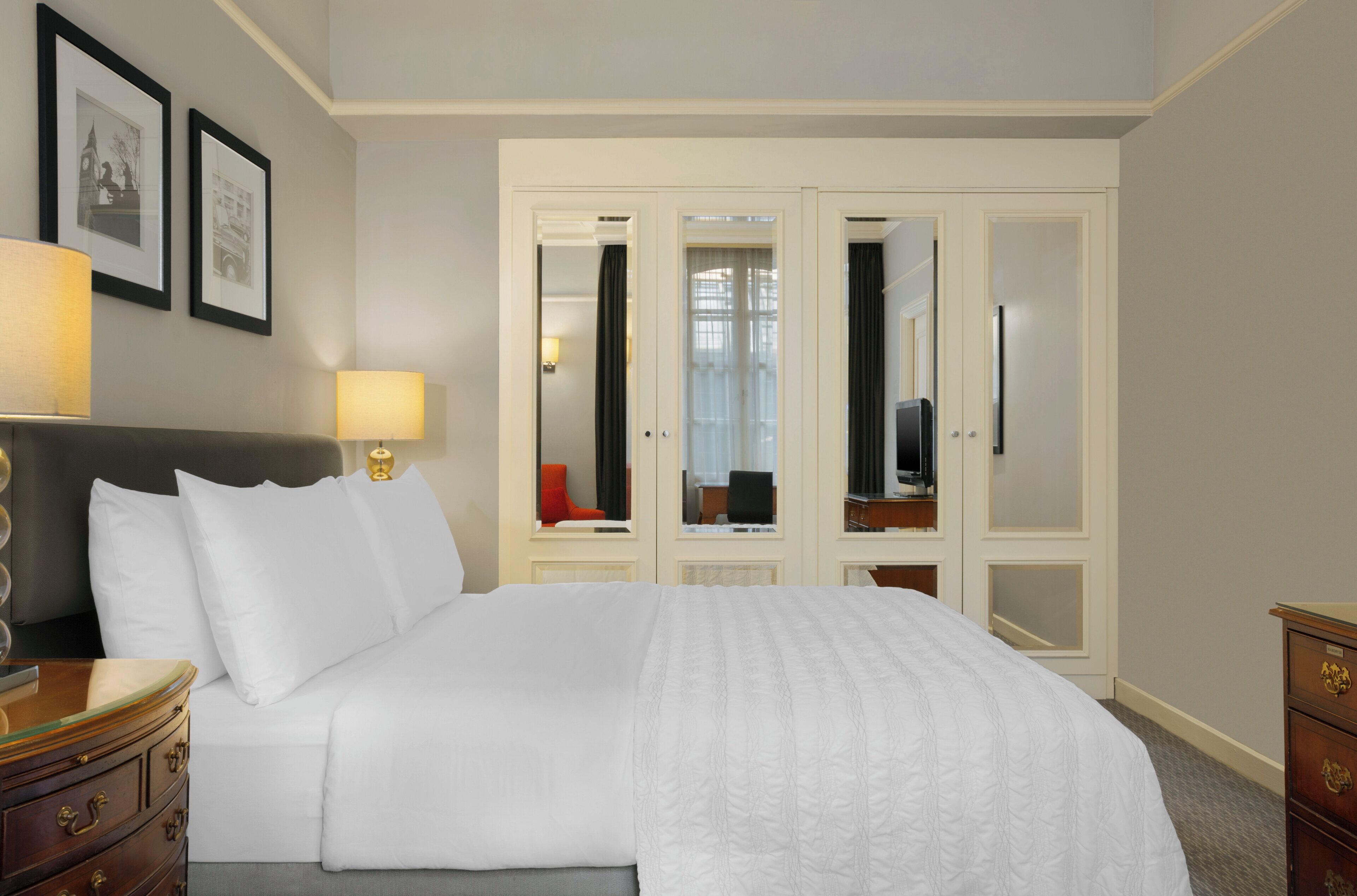 A hotel room with a large bed, a nightstand, a dresser, a mirror, and a wardrobe with a mirror.