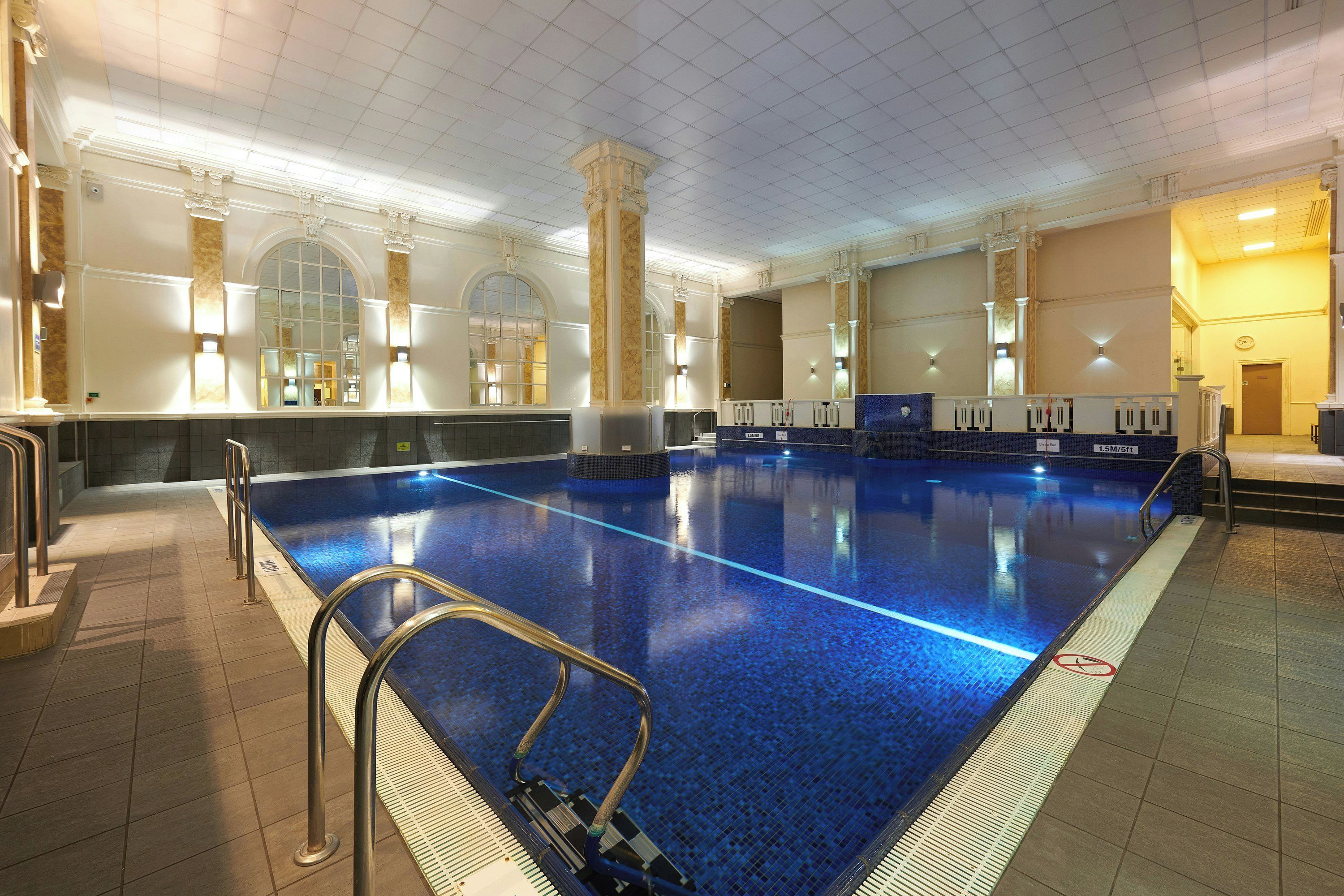 A large indoor swimming pool with clear blue water, surrounded by a tiled floor and walls.
