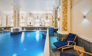 A large indoor swimming pool with a jacuzzi, wooden lounge chairs, and classical architecture. - The Dilly (London)