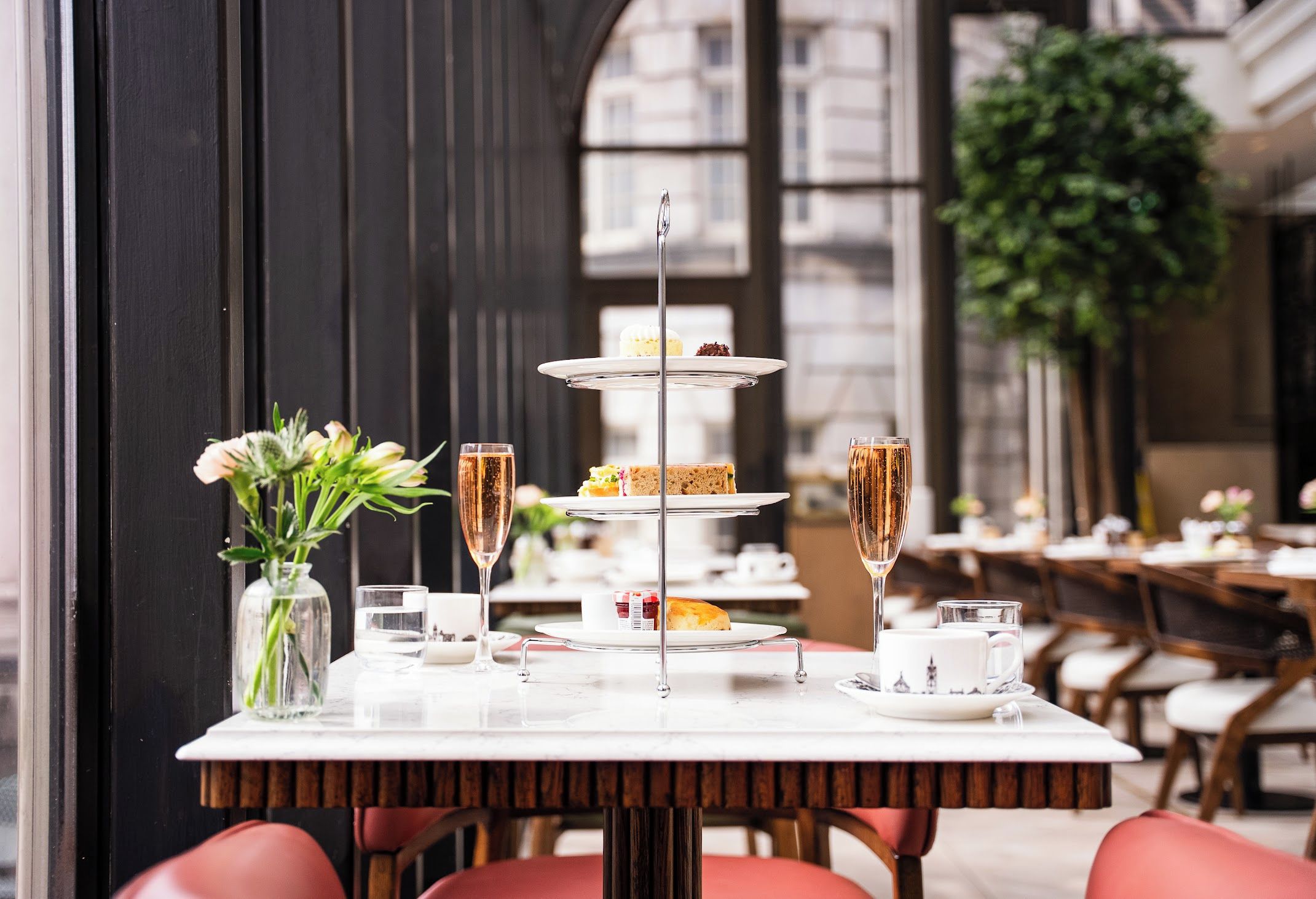 A table set for a meal with a three-tiered dessert stand, a vase with flowers, and glasses of a clear beverage.