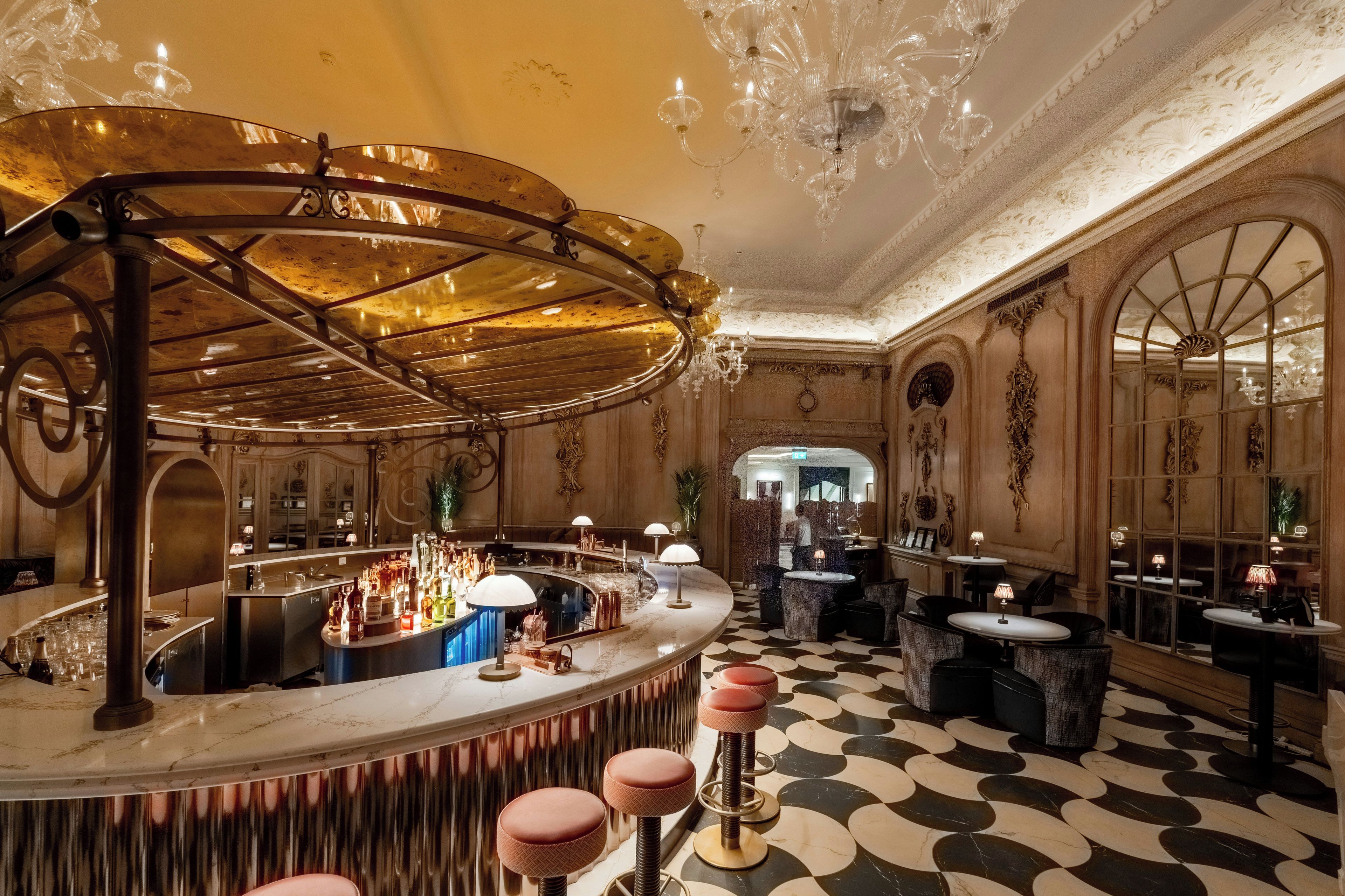 A bar area with a curved counter, stools, and a chandelier.