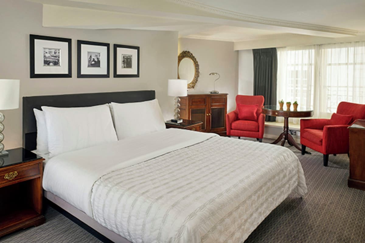 A hotel room with a large bed, two red armchairs, a wooden nightstand, a desk, and a mirror.