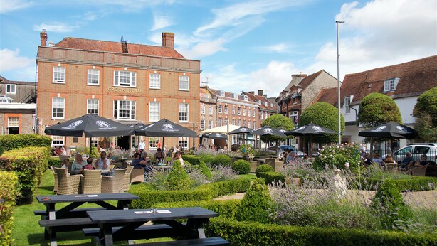 A courtyard with outdoor seating and umbrellas, surrounded by well-maintained hedges and plants. - Crown Hotel (Blandford Forum)
